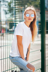 Wall Mural - Girl wearing white t-shirt, glasses and leather jacket posing against street , urban clothing style. Street photography