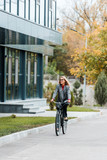 Fototapeta  - attractive businesswoman in coat and glasses smiling and riding bike