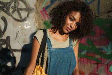 Wall Mural - African woman walking outdoors with bag by street.