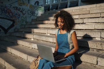 Poster - Pretty young african woman using laptop computer by street.