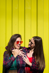 Portrait of two young happy women friends standing outdoor over yellow wall