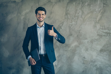 Photo of cheerful toothy positive man holding laptop showing you thumb up with stubble near empty space isolated grey color background