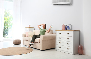 Canvas Print - Happy young woman switching on air conditioner with remote control at home