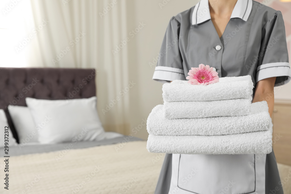 Chambermaid with stack of fresh towels in hotel room, closeup. Space for text - obrazy, fototapety, plakaty 