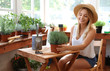 © New Africa - Young woman taking care of home plants at wooden table in shop