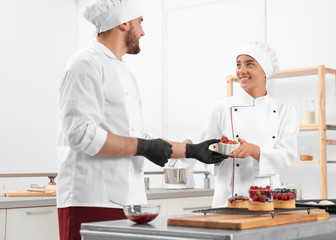 Wall Mural - Pastry chefs preparing desserts at table in kitchen