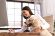 © New Africa - Young woman working at home office and stroking her Golden Retriever dog