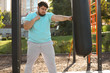 © New Africa - Young overweight man kicking heavy bag on sports ground