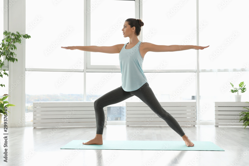 Young woman practicing warrior asana in yoga studio. Virabhadrasana pose - obrazy, fototapety, plakaty 