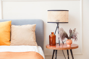 Wall Mural - Stylish lamp on wooden nightstand next to flower in big glass vase in scandinavian bedroom interior