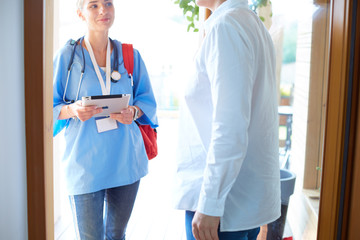 Wall Mural - Female doctor with clipboard during home visit while entering house