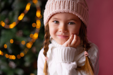 beautiful little girl in the hat sitting near presents and christmas tree. bokeh lights on the backg