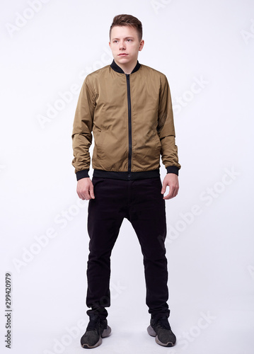 Fotomural Young man in jeans, shiny nylon gold bomber jacket on white background
