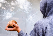 Child Holds A Stone To Throw It Against A Glass And Break A Window.