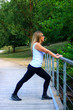 © Bruno - Long-haired blonde girl doing stretching in a park near a lake. Trees and vegetation in bokeh background. Woman doing fitness exercises at the water's edge.