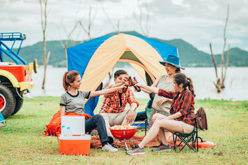 group of friends having barbecue and clinking bottle of beers while camping