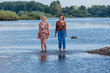© Smile - Two pretty sisters standing in river next to the shore on a cloudy windy summer day, having fun and laughing.