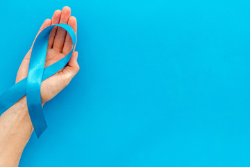 Wall Mural - Blue ribbon in hands as symbol disease control on blue background top view space for text