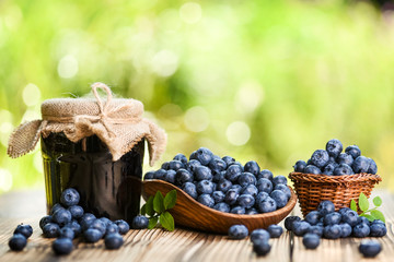 Wall Mural - Blueberries in wicker basket on old wooden table. Blueberry jam or marmelade in glass bottle.