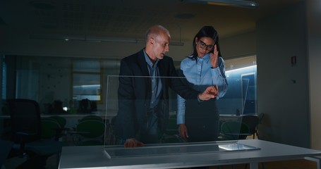 Two designers are using a futuristic sophisticated technology screen with augmented reality holograms for a new worldwide global project realization in an office.