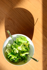 top view of  fresh green leaf salad with two spoons in round white bowl