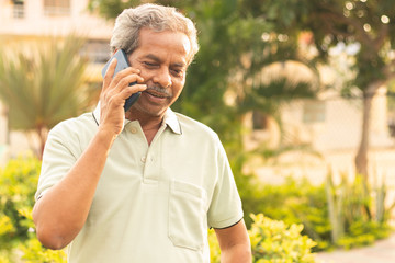 healthy senior asian on phone outdoor green park - elder man busy in mobile - happy male parent talk