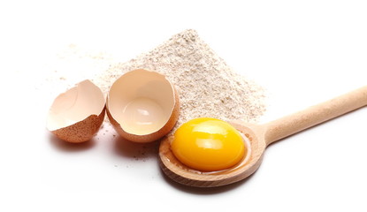 Cracked egg with yolk, rye flour pile and wooden spoon isolated on white background