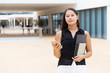 © Mangostar - Pensive female student holding notebooks and papers, texting message. Young Latin woman standing near city building, using mobile phone, looking at camera. Modern student concept