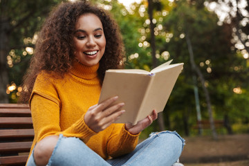 Beautiful curly woman sit in park outdoors reading book.