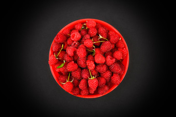 Wall Mural - Raspberries in a red plate on a black background. Bowl with fresh raspberries on a pink background. Copy space. Minimal concept. hard light.