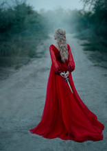Dangerous Blonde Queen In Red Fashion Lush Dress Hides A Dagger Behind. Backdrop Dark Fantasy Forest In Fog. Concept Revenge Conspiracy Betrayal. Halloween Party. Turned Away Without Face. Long Train