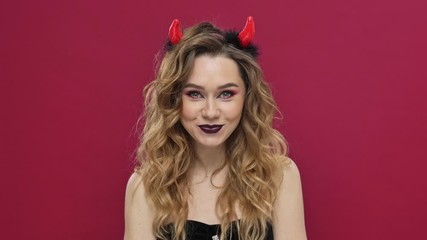 Poster - Pretty devil woman in carnival costume winking and pointing at the camera isolated over red wall background