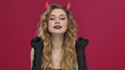 Poster - Beautiful and crazy devil woman in carnival costume flirt to the camera and bite isolated over red wall background 