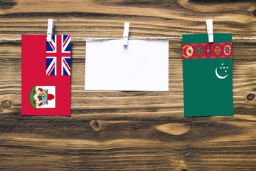 Hanging flags of Bermuda and Turkmenistan attached to rope with clothes pins with copy space on white note paper on wooden background.Diplomatic relations between countries.