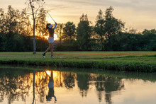 Healthy Sport. Asian Sporty Woman Golfer Player Chips And Swing Golf On The Green Sunset Evening Time, She Presumably Does Exercise.  Healthy Lifestyle Concept.