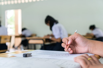 Asian Students holding pencil in hand doing multiple-choice quizzes or testing exams answer sheets exercises on old wood table In secondary school, college university classroom in education concept