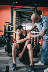 attentive african american doctor touching injured shoulder of young sportsman