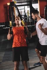 Wall Mural - attentive trainer supporting young african american athlete pulling up on suspension trainer