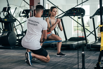 back view of personal trainer controlling attractive sportswoman exercising with resistance band
