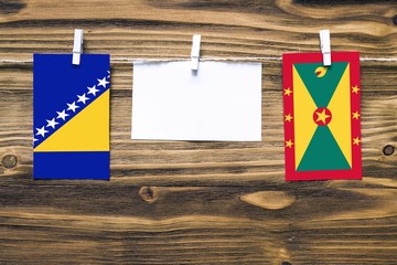 Wall Mural - Hanging flags of Bosnia Herzegovina and Grenada attached to rope with clothes pins with copy space on white note paper on wooden background.Diplomatic relations between countries.