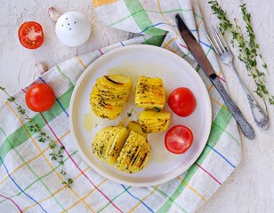 Hasselback potatoes on a white clay plate on a light concrete background. Potato recipes. Thanksgiving Day. Scandinavian cuisine. Top view.