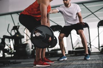 cropped view of trainer supporting american sportsman lifting barbell