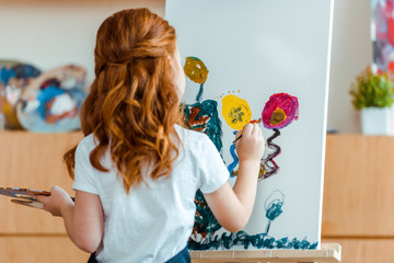back view of redhead child painting on canvas in art school