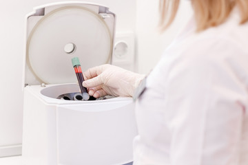Wall Mural - Female cosmetologist uses medical plasma centrifuge for plasma lifting procedure in cosmetology clinic. Young nurse in laboratories starts on device for mixing process of separation plasma from blood