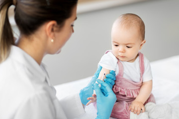 Wall Mural - medicine, healthcare and vaccination concept - female pediatrician doctor or nurse with syringe making injection of vaccine for baby girl patient at clinic or hospital