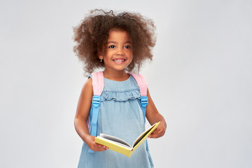 Wall Mural - childhood, school and education concept - happy little african american girl with book and backpack over grey background