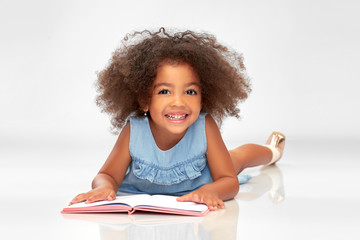 Wall Mural - childhood, school and education concept - happy smiling little african american girl reading book over grey background