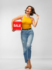 Sticker - shopping and people concept - happy smiling young woman in mustard yellow top and jeans with sale sign posing over grey background