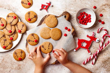 Wall Mural - Cooking Christmas gingerbread.  Child's hand decorating red nosed reindeer cookies with chocolate buttons and melted chocolate. Festive homemade decorated sweets