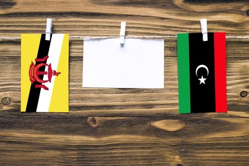 Wall Mural - Hanging flags of Brunei and Libya attached to rope with clothes pins with copy space on white note paper on wooden background.Diplomatic relations between countries.